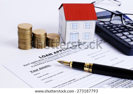 Mortgage loans concept with close up fountain pen and loan application form and coins stack and paper house and eyeglasses on calculator