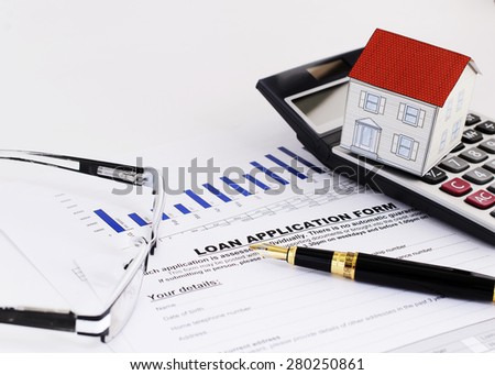 close up of fountain pen and loan application form and paper house on calculator and eyeglasses for Home loans concept