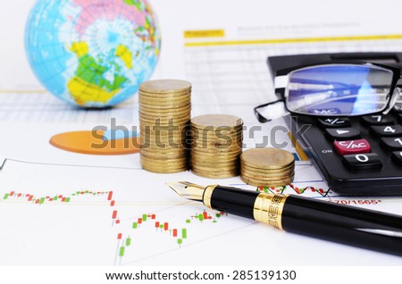 Stock investment concept with fountain pen and coins stack and calculator and eyeglasses on stock chart report