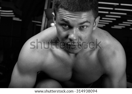Young strong man pushed, having rested on the dumbbell. The muscles on his arm stretched and embossed. Young muscular athlete trains in the gym. black and white