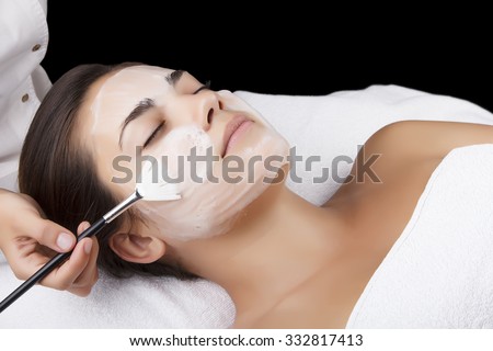 Young pretty woman receiving treatments in beauty salons. Young beautiful dark-haired woman in the office beautician lying on the couch. Facial cleansing foam using. Isolated black.