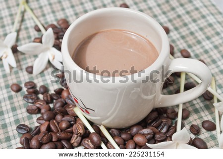 Cup of coffee on the fabric, with white flowers and coffee beans.