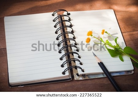 Notebook with black pencil, white flowers on wooden table