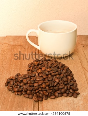 coffee mug and heart symbol made of coffee beans in love on wooden table, vintage tone style