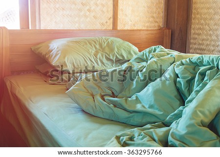 green pillow and blanket with wrinkle messy on bed in vintage wooden bedroom with lighting upper left side, from sleeping in a long night winter.