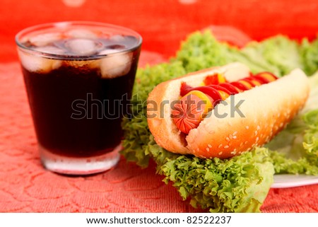 black drink and hot dog over lettuce over orange table