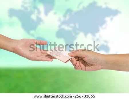 Hand handing over money to another hand  on blurred abstract nature background