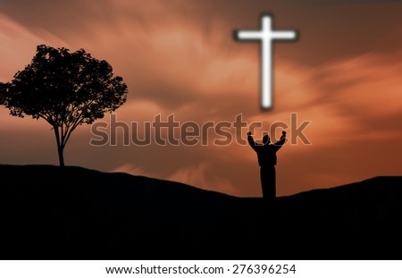 A man standing on a nature with hands in prayer with a cross.