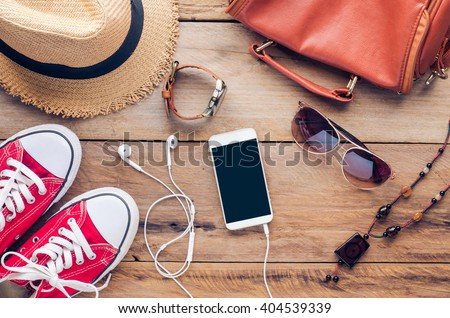 Accessories for teenage girl on her vacation. Straw hat, stylish sunglasses, brown leather bag, red shoes and costume on wooden floor.