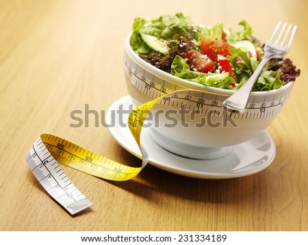 A bowl of mixed salad with a tape measure for healthy eating on a wooden background.