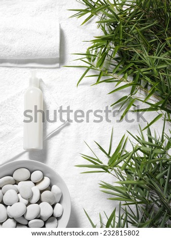 Bamboo leaves and towel with a massage lotion on white towel background with pebbles in a bowl, copy space for a health and leisure business.