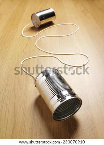 Two tin cans joined with a cord on a wooden background for primitive communication with copy space.