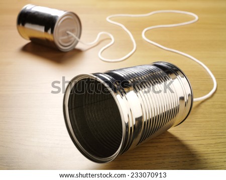 Two tin cans joined with a cord on a wooden background for primitive communication.