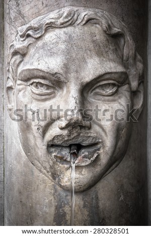 Detail of an old Italian fountain whose jet of water flows from the mouth of a face carved in marble.