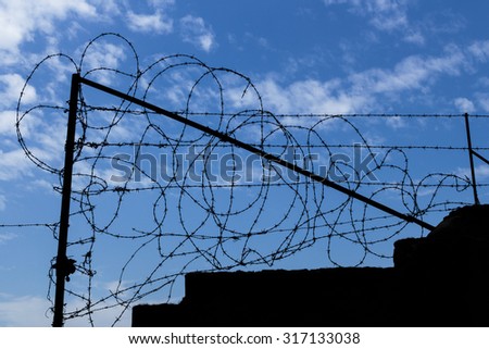 Barbed wire fence with blue sky and clouds in the background.