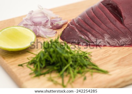 Close up of fresh and raw pig\'s liver with green lime, red onion and sour lemon on chopping block for food preparation