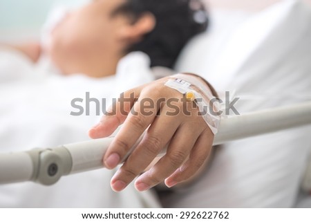 Female patient with IV drip needle piercing on hand, lying on bed in hospital for medical care background