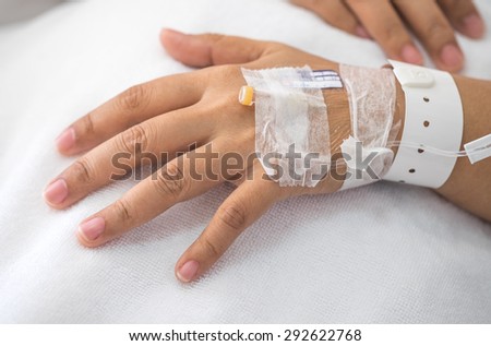 Hand with IV drip needle, patient lying on bed in hospital for medical care background