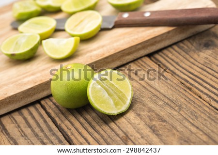 Fresh cut green lime or lemon with chopping board and knife on wood background