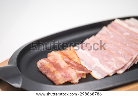 Grilled or barbecued fresh and sliced bacon or pork belly on black metal plate for breakfast or appetizer with white background
