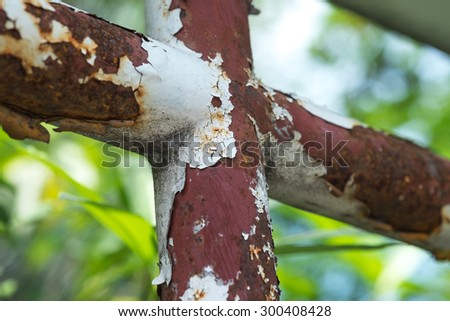 Rustic iron pipe in cross shape with paint peeling off against green background