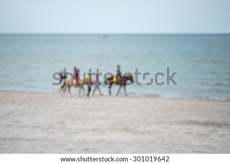 De focused or blurred image of people riding horses on the beach in the evening