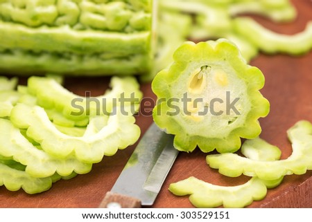 Fresh and raw green bitter gourd cut in pieces with knife on cutting board for food ingredient background