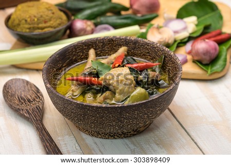 Delicious hot and spicy green curry chicken soup in bowl with herbs and spices on wooden table for local Thai food