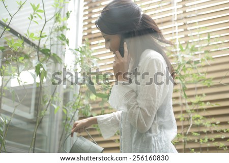 Side profile of a young woman talking on a mobile phone and watering plants