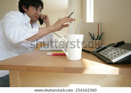 Side profile of a young man using a laptop and talking on the telephone