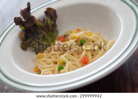 Dish of spaghetti carbonara with carrots, corn, peas, shrimp.