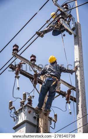 Bangkok, Thailand - May 16, 2015:  Electrician looking at co-worker while working on the electricity pole