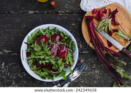 Preparing salad with dandelions, red beets and red onion. Fresh organic vegetables. Food dark background. Healthy herbs from garden