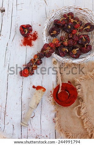 Overhead view of colorful dried ground peppers in basket spilling onto an old aged scored wooden surface in a country kitchen with a vintage sieve. Color brand
