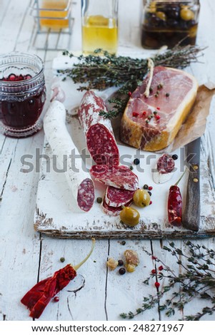 Cold meat plate of salchichon sausages and ham served with wine and red hot peppers on white wooden cutting board. See series. Natural meat concept.