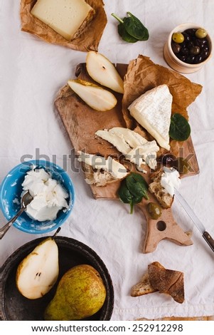 Close-up of a slice of wholemeal bread with variety cheeses and butter with sliced organic pear and rustic knife. Served on a dark rustic wooden table, on a natural napkin. Antipasti food concept.