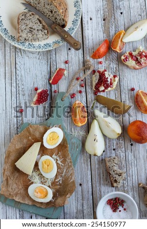 Still life of a antipasto of toast with cheese, clementine, pomegranate, pear  on a rustic table with whole grain bread. Meal is served on a table with boiled eggs. Authentic natural food.