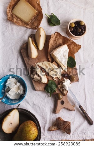 Close-up of a slice of wholemeal bread with variety cheeses and butter with sliced organic pear and rustic knife. Served on a dark rustic wooden table, on a napkin natural. Antipasti food concept.
