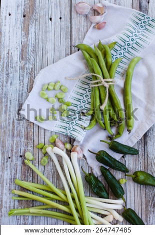 Fresh and organic vegetables of garden. Green string beans, green peppers, and bunch of garlic over a napkin texture, on a vintage wooden  table. Top view.