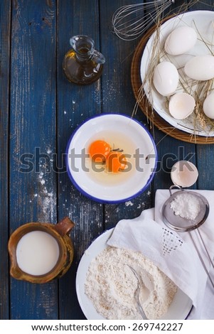Preparing of pancakes. Baking background with eggs, flour and pottery pitcher milk, bottle oil olive. Top view. Rustic style.