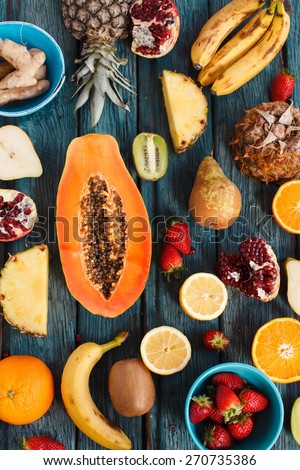 Overhead of fresh various fruits raw produce on rustic blue background, papaya, orange, lemon, strawberries, kiwi, pomegranate, ginger, pineapple, pear, banana.