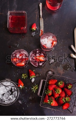 Vintage basket with strawberry, cups of homemade strawberry lemonade and ice cubes, strawberry jam over a dark background. See series.
