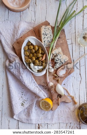 Mediterranean snacks produce gorgonzola cheese, green olive marinated with young garlic and olive oil , over on vintage cutting board and linen napkin from above. Dinner food concept.