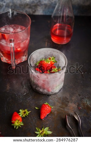 Ice cup with strawberry fruit served on dark vintage surface with freshness syrup of bottle and pitcher of water with fruit. See series.