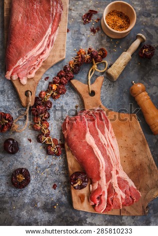 Many cut steaks for beef with dried Cayenne pepper and kitchen tools over on blue dark surface. Top view. Rustic style.