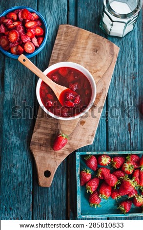 Rustic atmosphere with homemade strawberry confiture with same fruits over on blue vintage table. Rustic style.