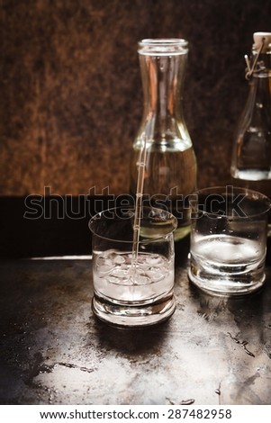Transparent drink with ice cubes over on dark metal table. Alcoholic or refreshing summer drink concept.