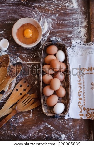 Country and real food concept. Vintage kitchen utensil with rustic basket of eggs and rustic embroidery linen napkin served on a moody wooden table from above. Rustic country image.