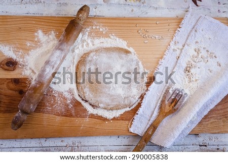 Roll out the whole grain dough from kitchen wooden table with oat flakes flour above the linen napkin. Rustic style.