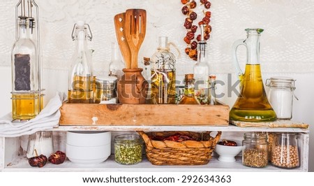 Assortment of spicy olive oils with herbs and spices in different bottles over kitchen shelves. Decorative and rustic kitchen interior.